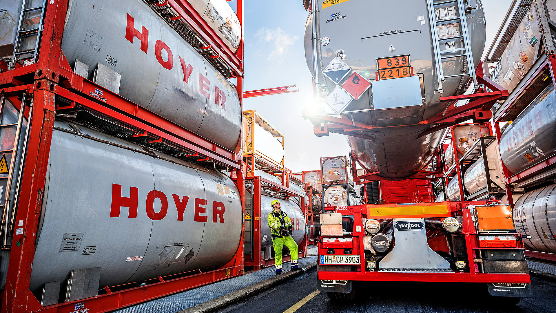 Chemie Ein LKW wird mit einem Tankcontainer der HOYER Group für chemische Produkte beladen. Ein Arbeiter in gelber Arbeitskleidung steht neben dem LKW und beobachtet den Vorgang.
