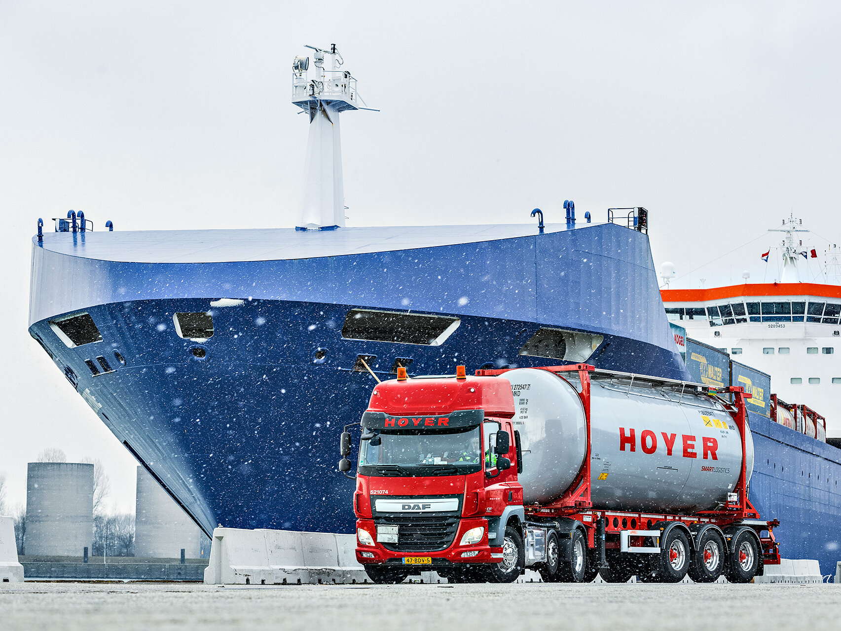 Integrierte Logistik HOYER Lkw mit Chemie-Tankcontainer smart logistics vor einem Schiff. Es schneit.